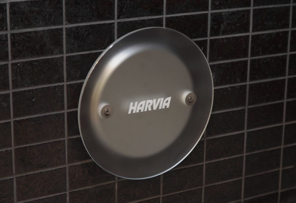 grey round steam nozzle with Harvia logo against a black checked bathroom tiles