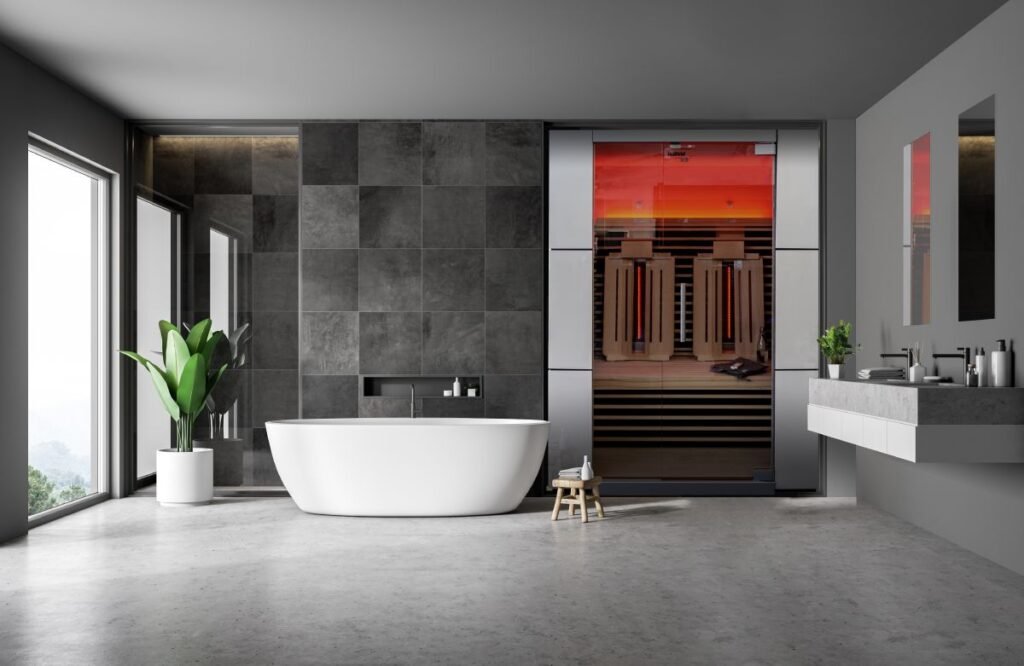 a full view of a luxurious bathroom with grey walls, white bathtub in the center, a plant in one corner and an infrared sauna on the other