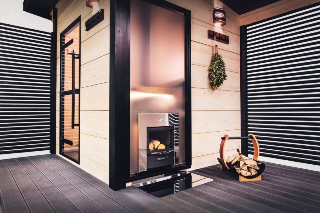 a black and light wood cabin in the outdoors with a black sauna bucket filled with timber