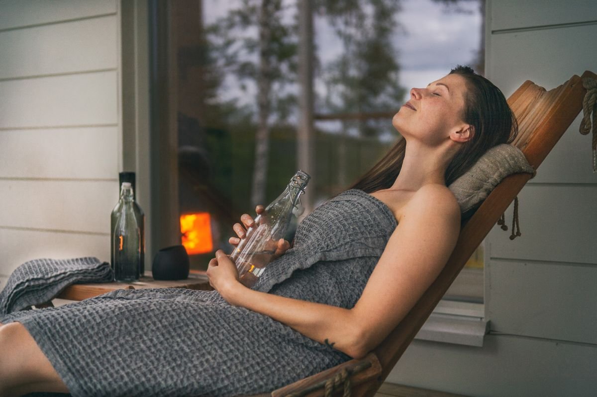 Woman relaxing in a lounge chair outside a sauna, wrapped in a towel